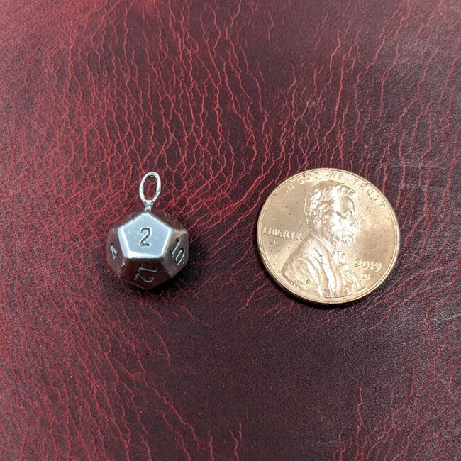 Sterling silver 12-sided die charm with "2" facing forward, next to a penny for scale.